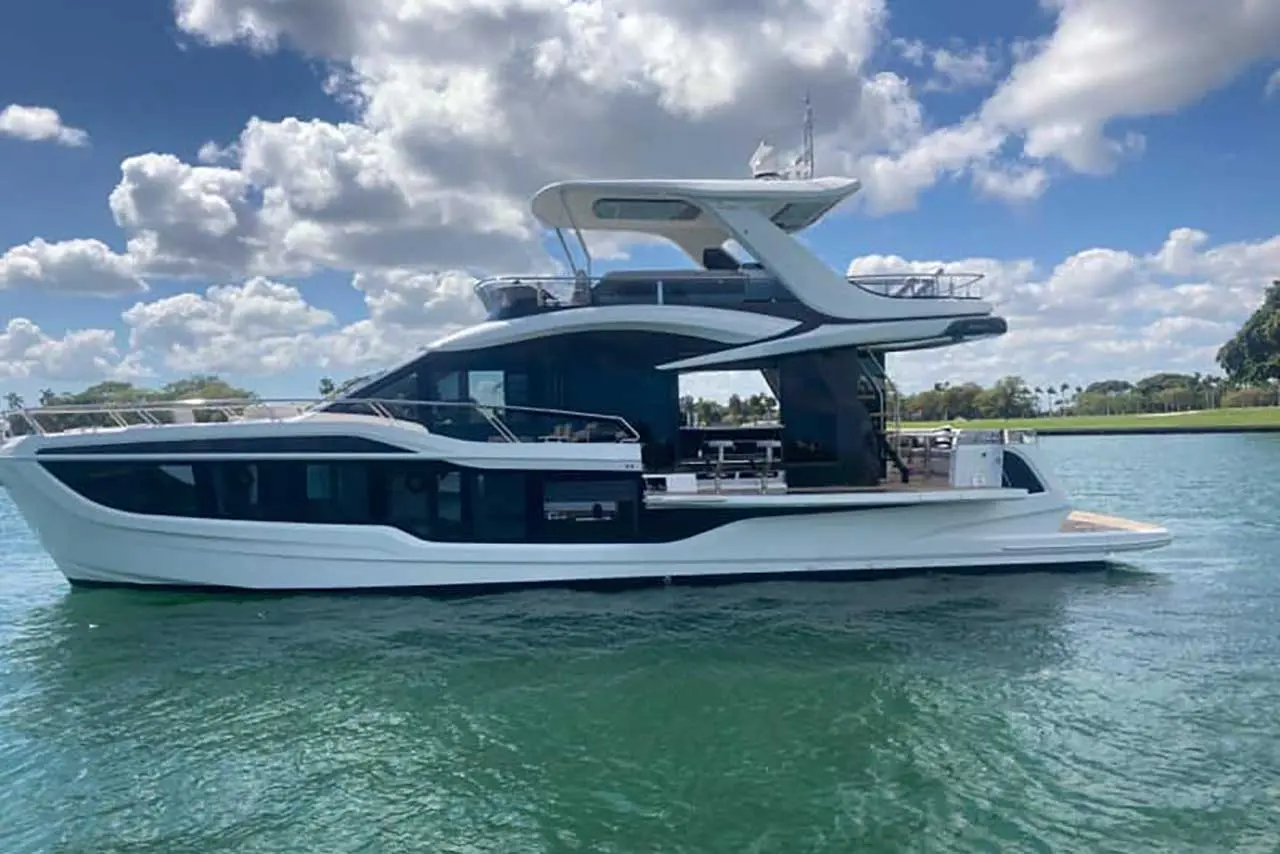 Luxury yacht anchored on clear blue water, with a modern design and cloud-filled sky in the background.