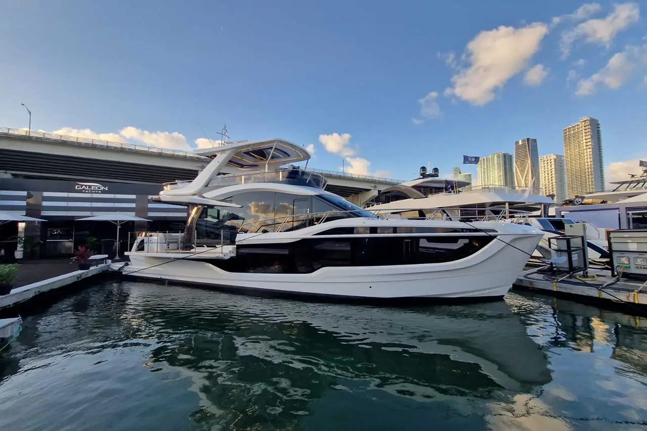 Luxury motor yacht at a marina near skyscrapers, featuring sleek design and docked alongside other boats under a blue sky.