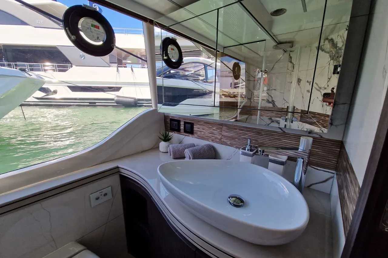 Stylish yacht bathroom featuring a modern oval sink, wooden accents, toiletries, and a view of boats on tranquil water.
