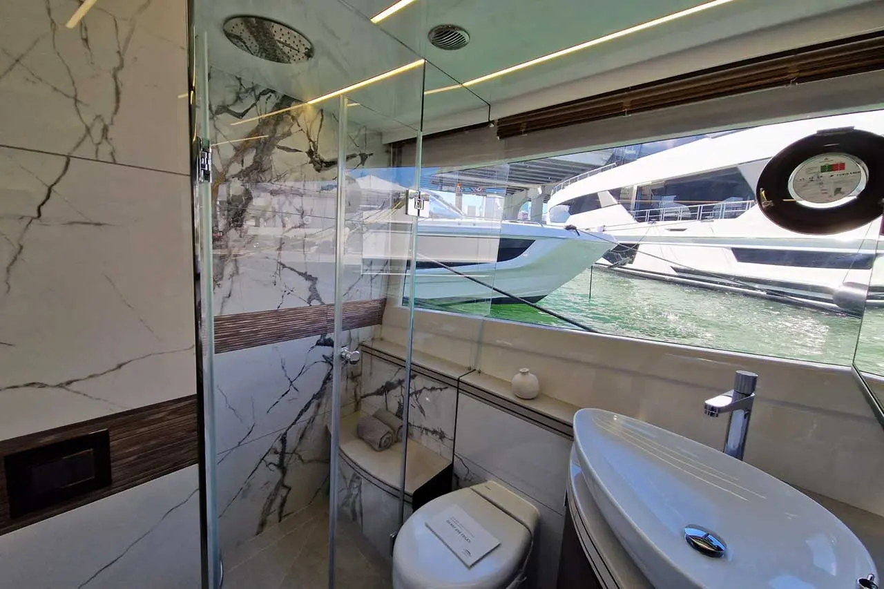 Luxurious boat bathroom featuring a glass shower, modern sink, and views of yachts through large windows. Elegant marble decor.
