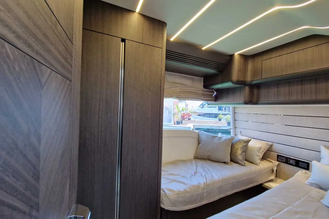 Modern boat interior featuring twin beds, gray cushions, wooden cabinetry, and natural light from windows.