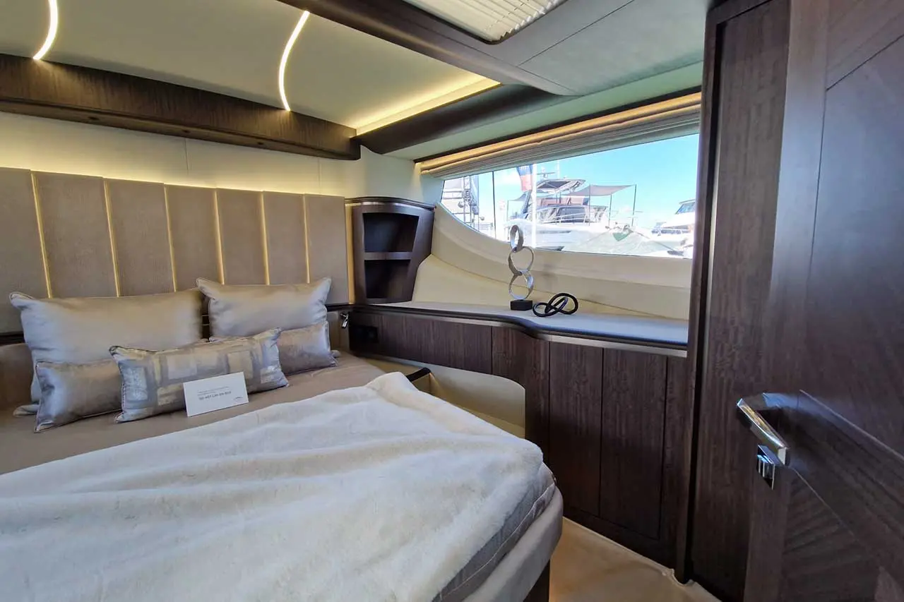 Luxury yacht interior featuring a stylish bed, decorative pillows, and a view of boats through a large window.