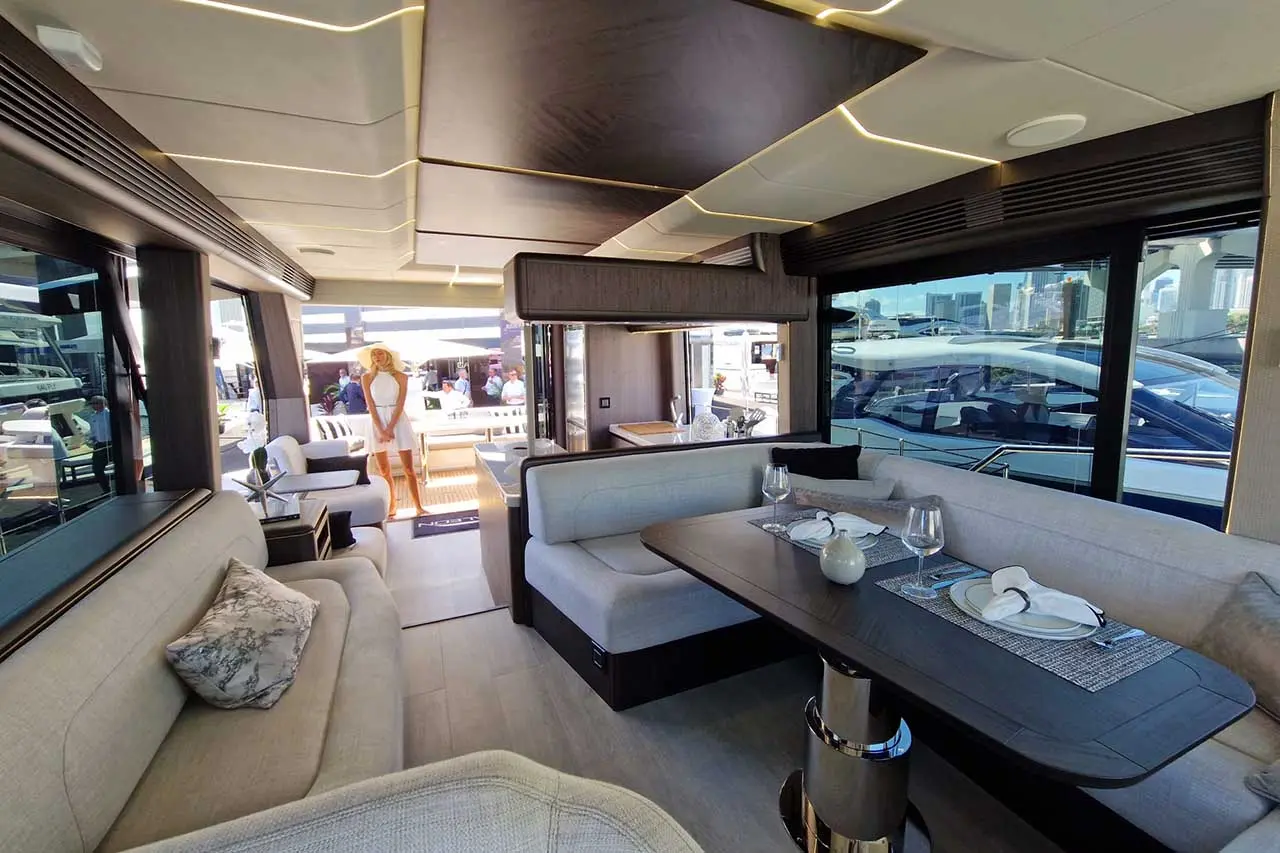 Luxury yacht interior featuring modern seating, dining table, and a woman in white dress overlooking the deck area.