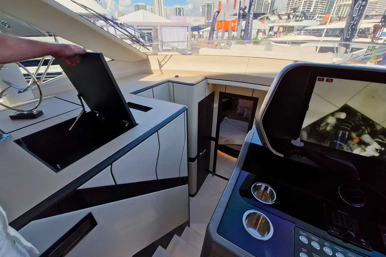 A person opens a hatch on a modern yacht, revealing stair access and a control panel with screens and buttons.