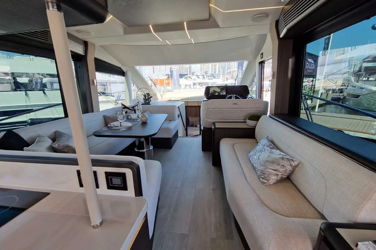 Modern yacht interior featuring a spacious lounge area, dining table, and panoramic windows with yacht views.