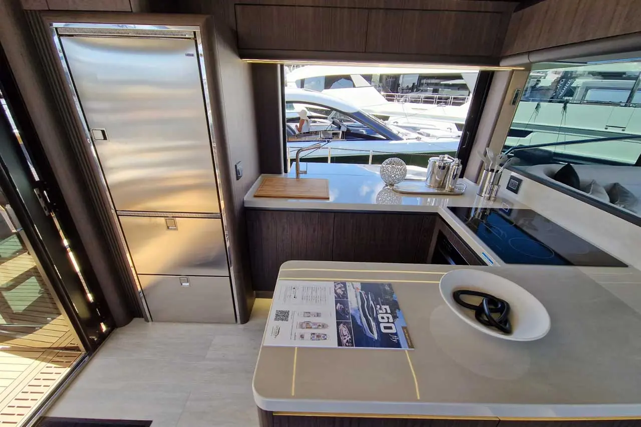 Modern yacht kitchen featuring sleek stainless steel appliances, countertop with brochure for a 560 yacht, and marina view.