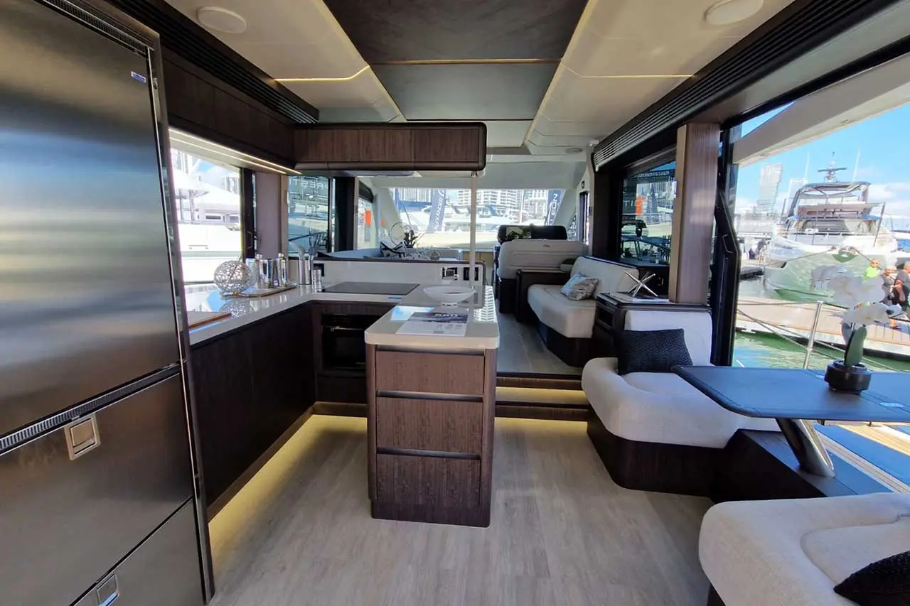 Modern yacht interior featuring a sleek kitchen, seating area, and large windows with a view of the marina.