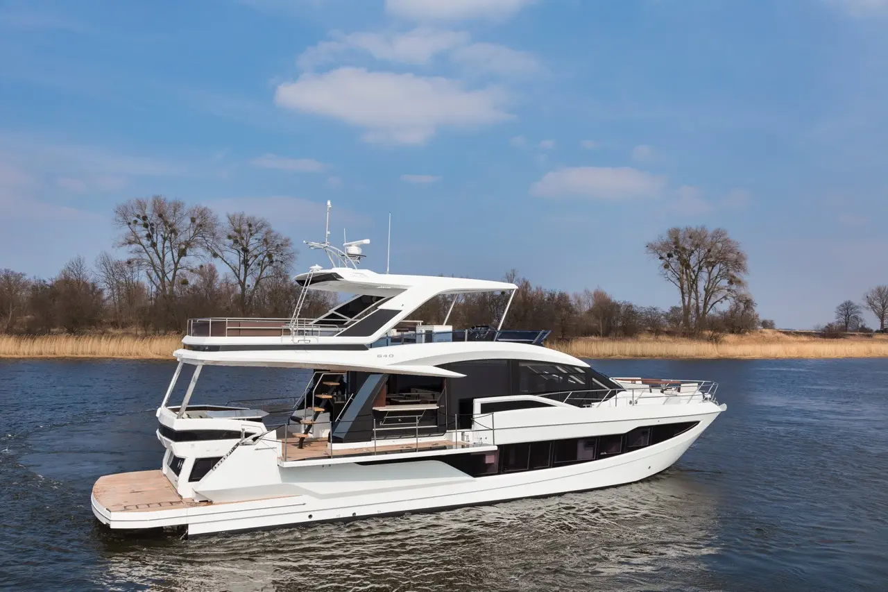 Luxury white yacht cruising on calm waters, with scenic trees and grassland in the background under a clear blue sky.