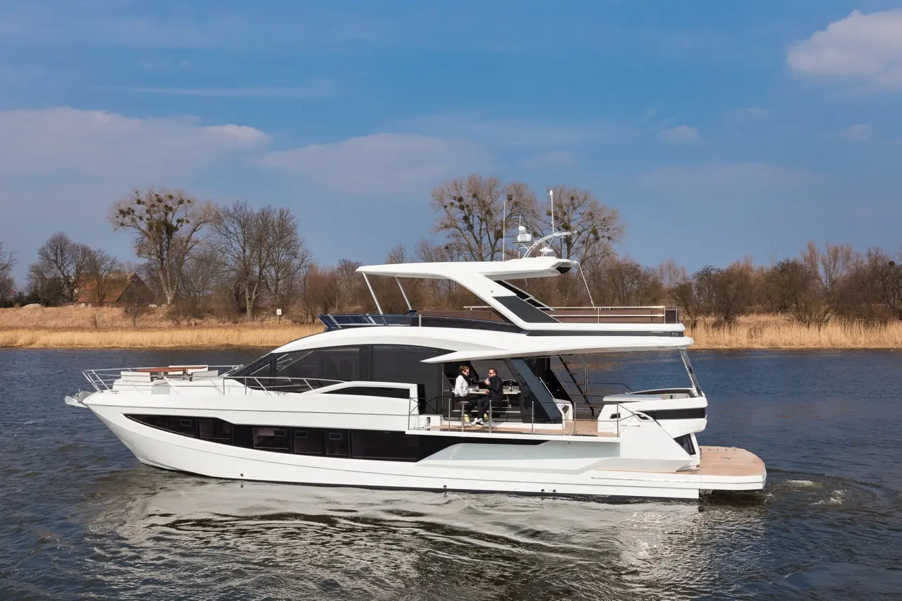 Luxury white motor yacht sailing on calm waters, with two people seated at a table on the deck under blue skies.