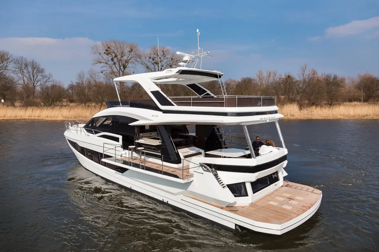 A sleek white yacht navigates calm waters, showcasing modern design with outdoor seating and a spacious upper deck.