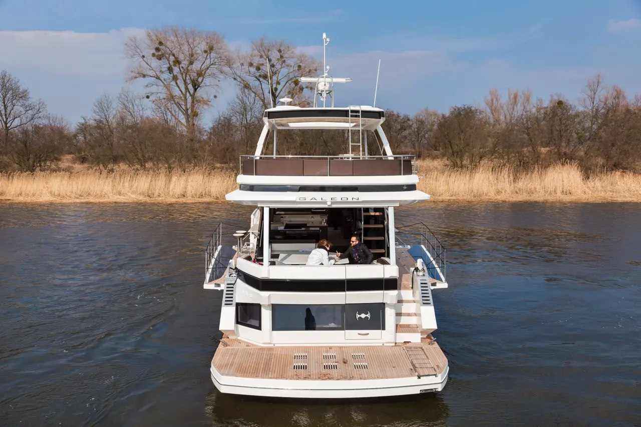 Luxury Galeon motor yacht moored on a river, with two people relaxing on the deck under a clear blue sky.