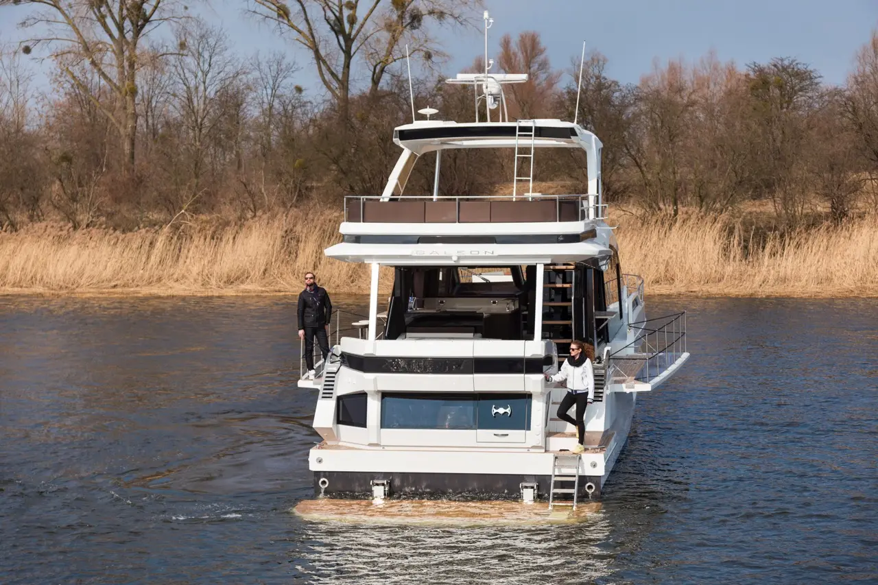 A luxury boat with two people on board, surrounded by water and reeds, featuring a stylish upper deck and modern design.