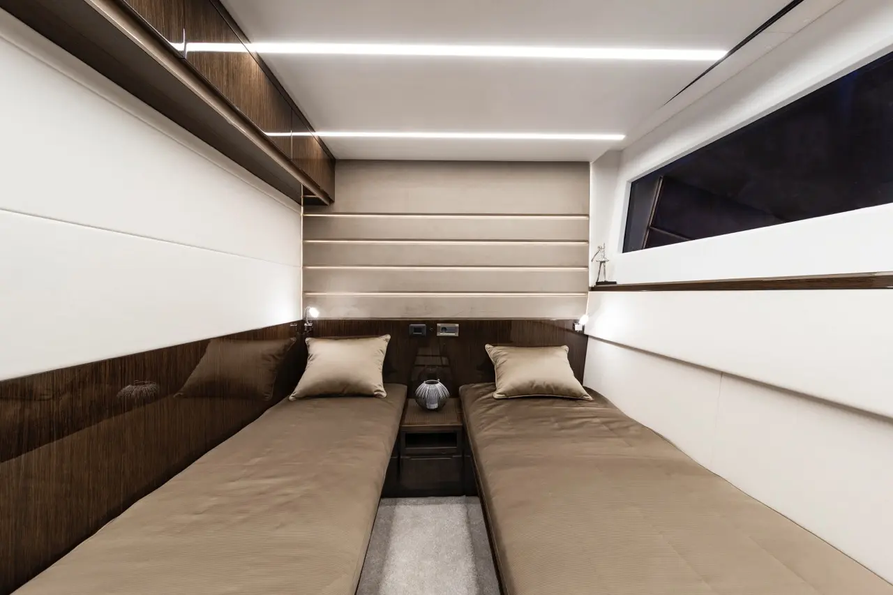 Sleek modern cabin with two single beds, warm brown tones, cushions, built-in lighting, and a small bedside table.