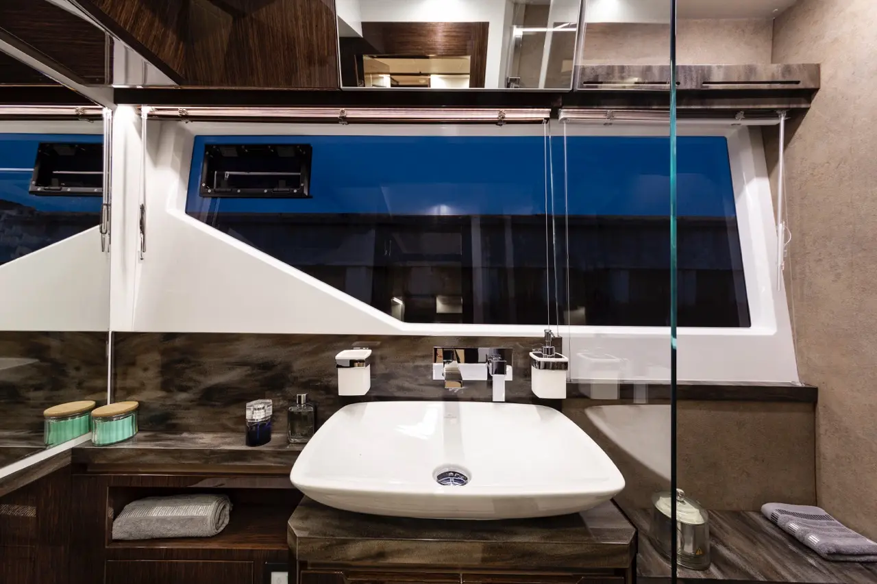 Modern boat bathroom featuring a stylish white basin, chrome fixtures, and blue view through a large glass window.