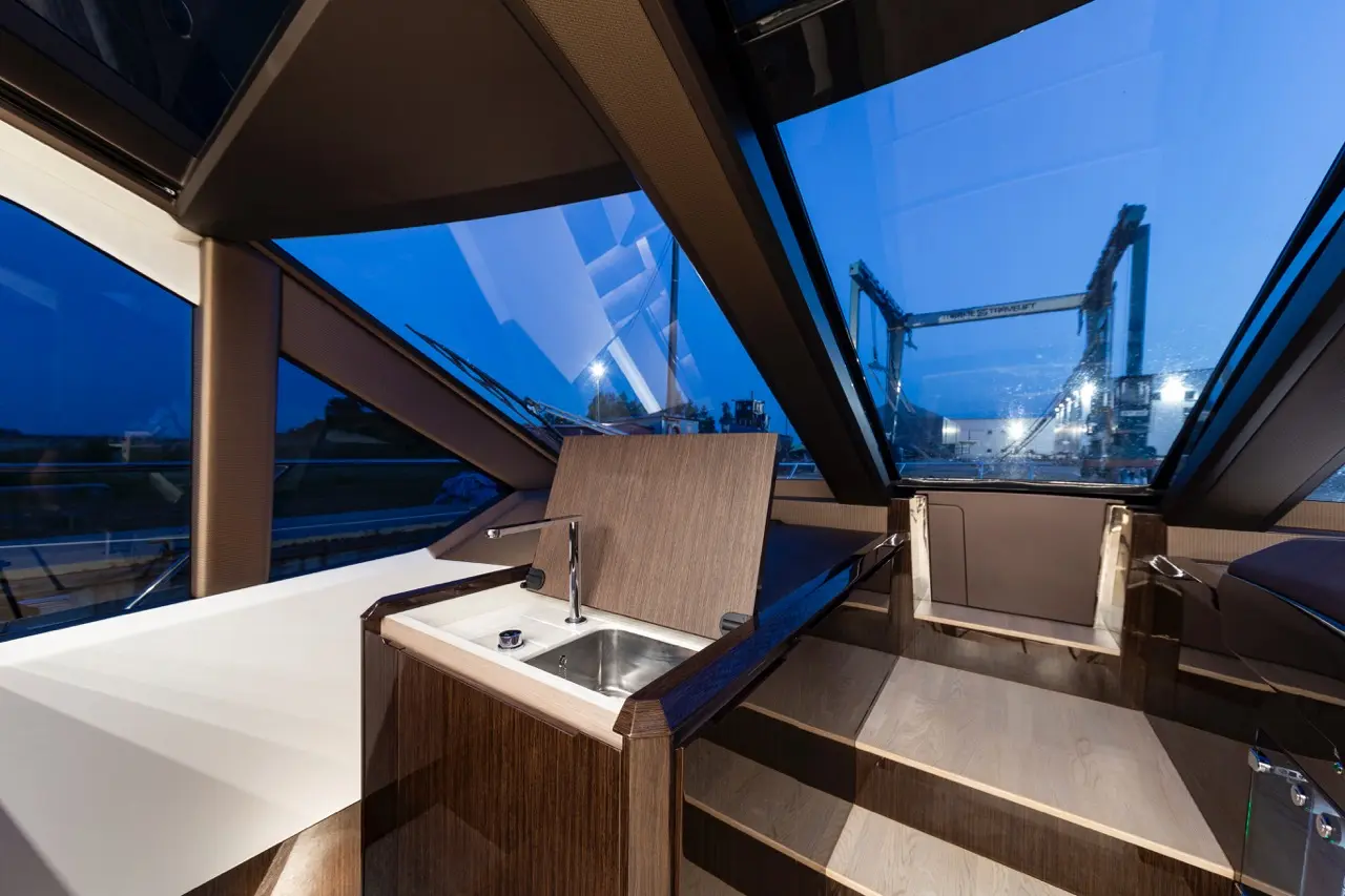 Interior of a modern boat showcasing a wooden kitchenette and stairs, with panoramic windows revealing a twilight dock view.