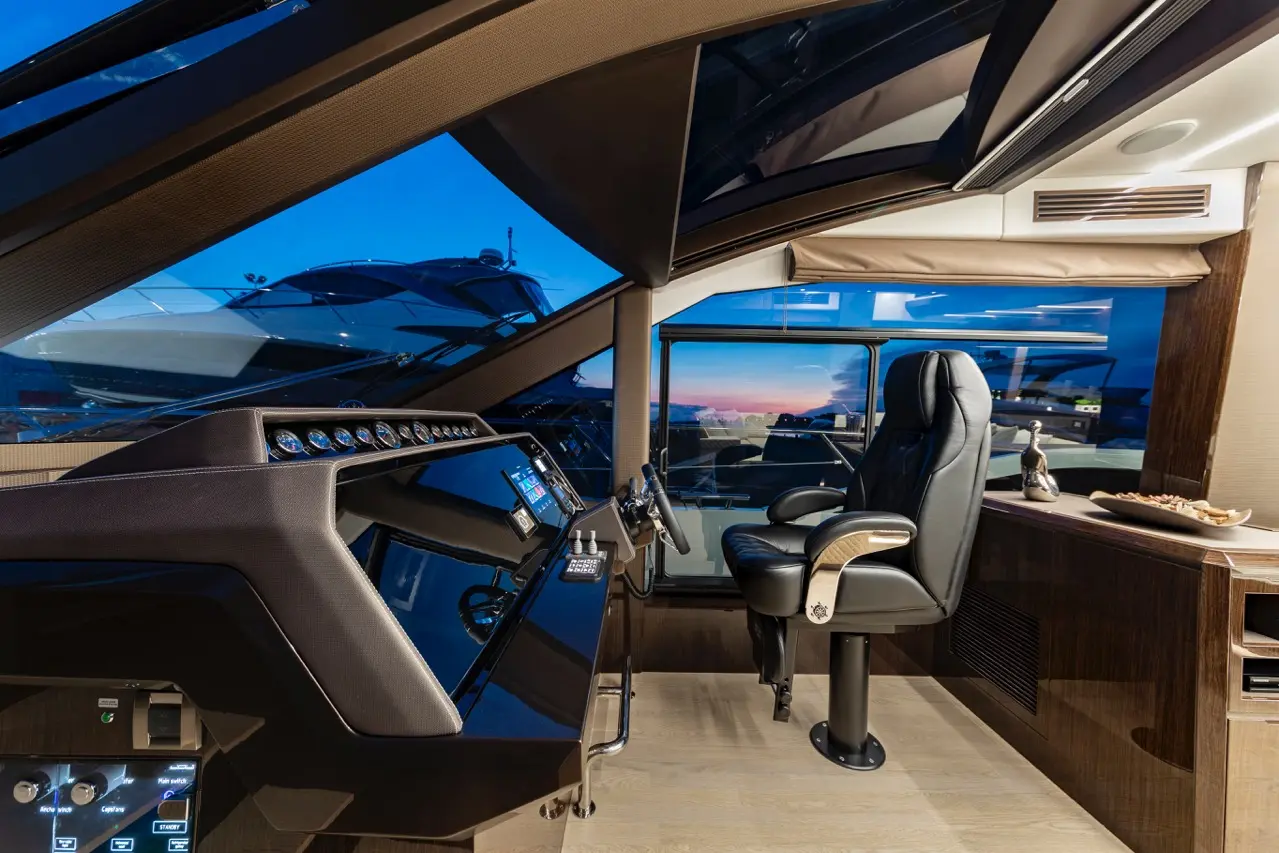 Luxury yacht interior with a sleek control panel, a plush captain's chair, and panoramic windows showcasing a sunset view.