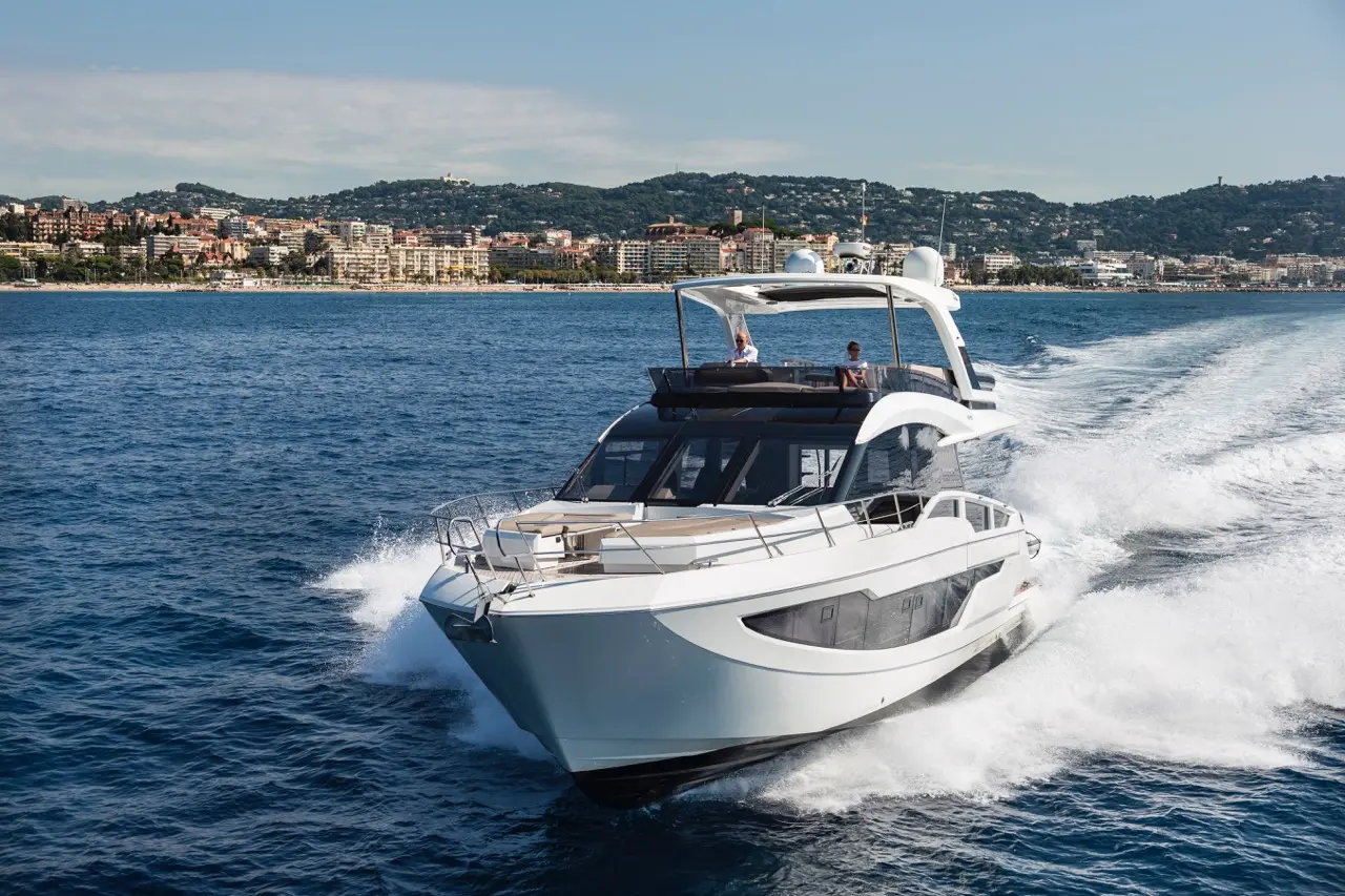 A modern yacht cruising through clear blue waters near a coastal town, showcasing luxury boating and scenic views.