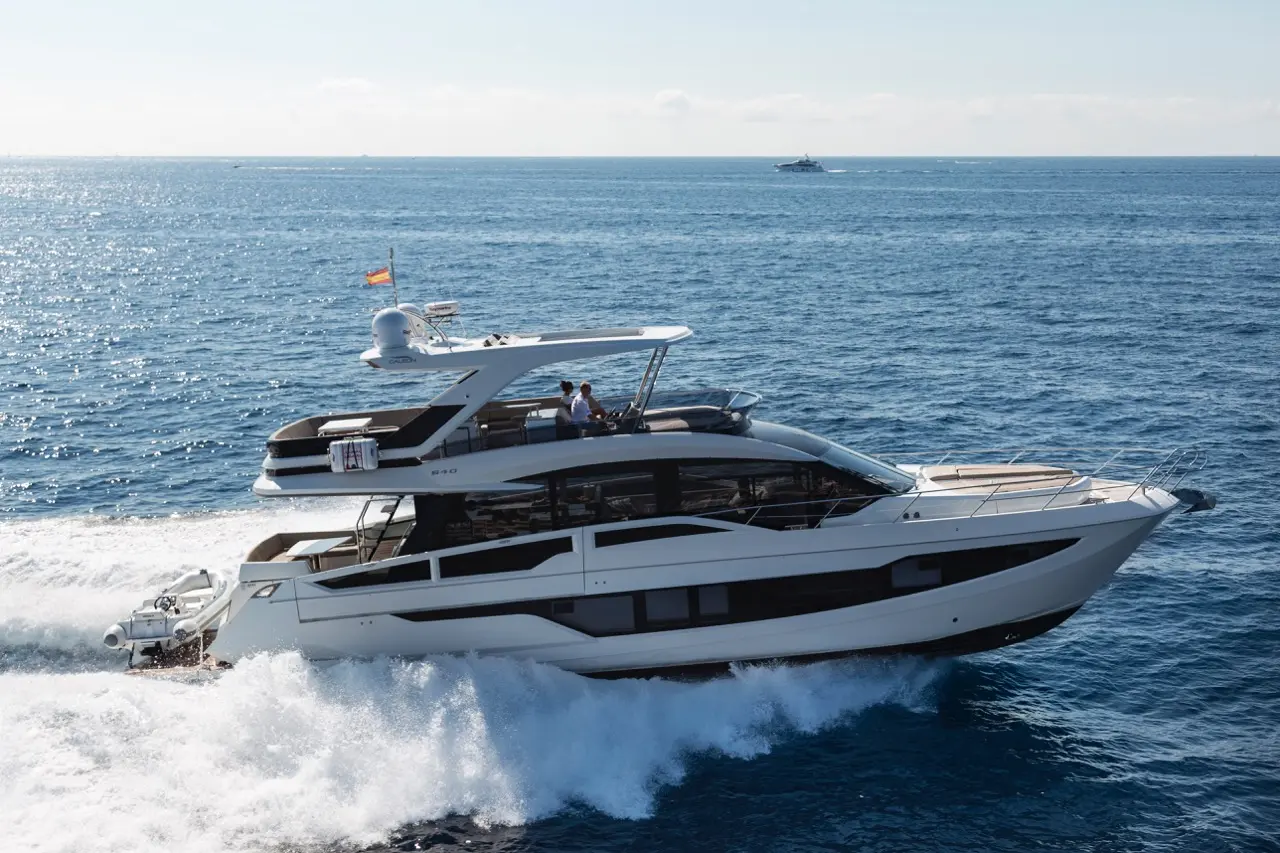 A sleek white luxury yacht cruises through azure waters, leaving a wake under a clear sky.