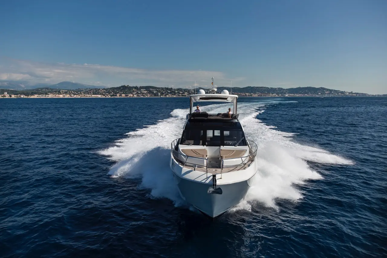 Luxury motorboat gliding through blue sea with spray, mountains and coastline visible in the background under clear skies.