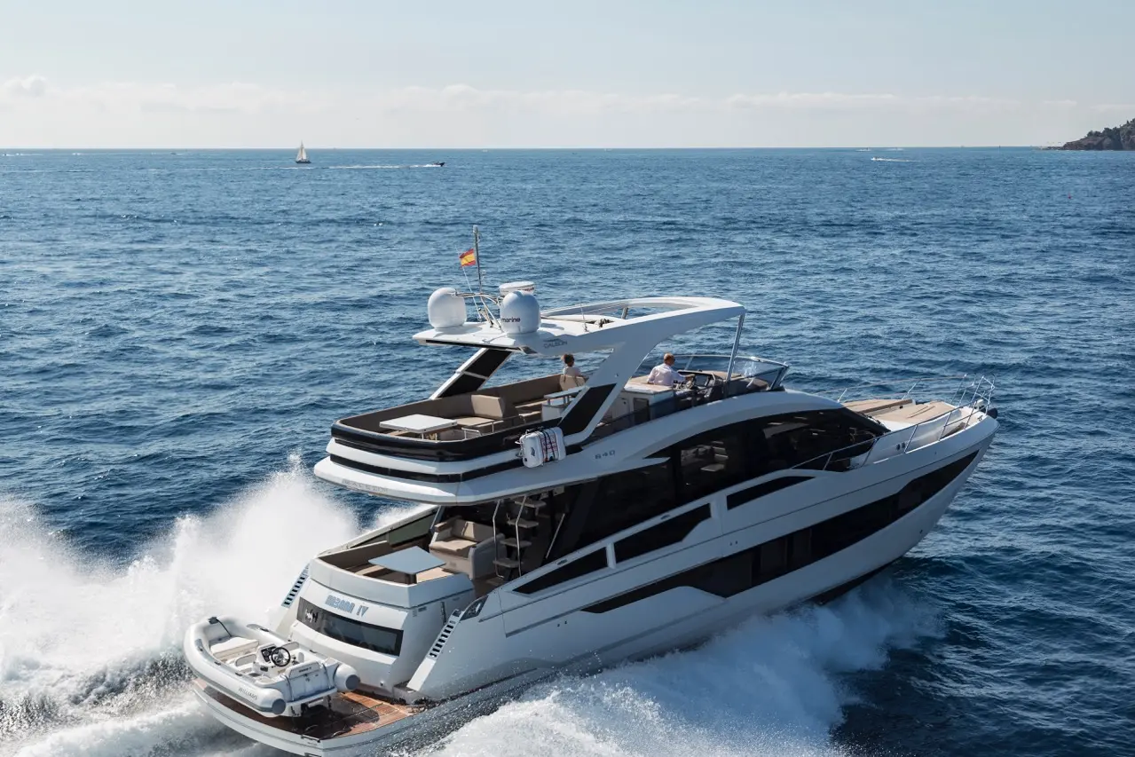 Luxury motor yacht cruising on blue waters, with sunbathers on deck and distant sailboats on the horizon.