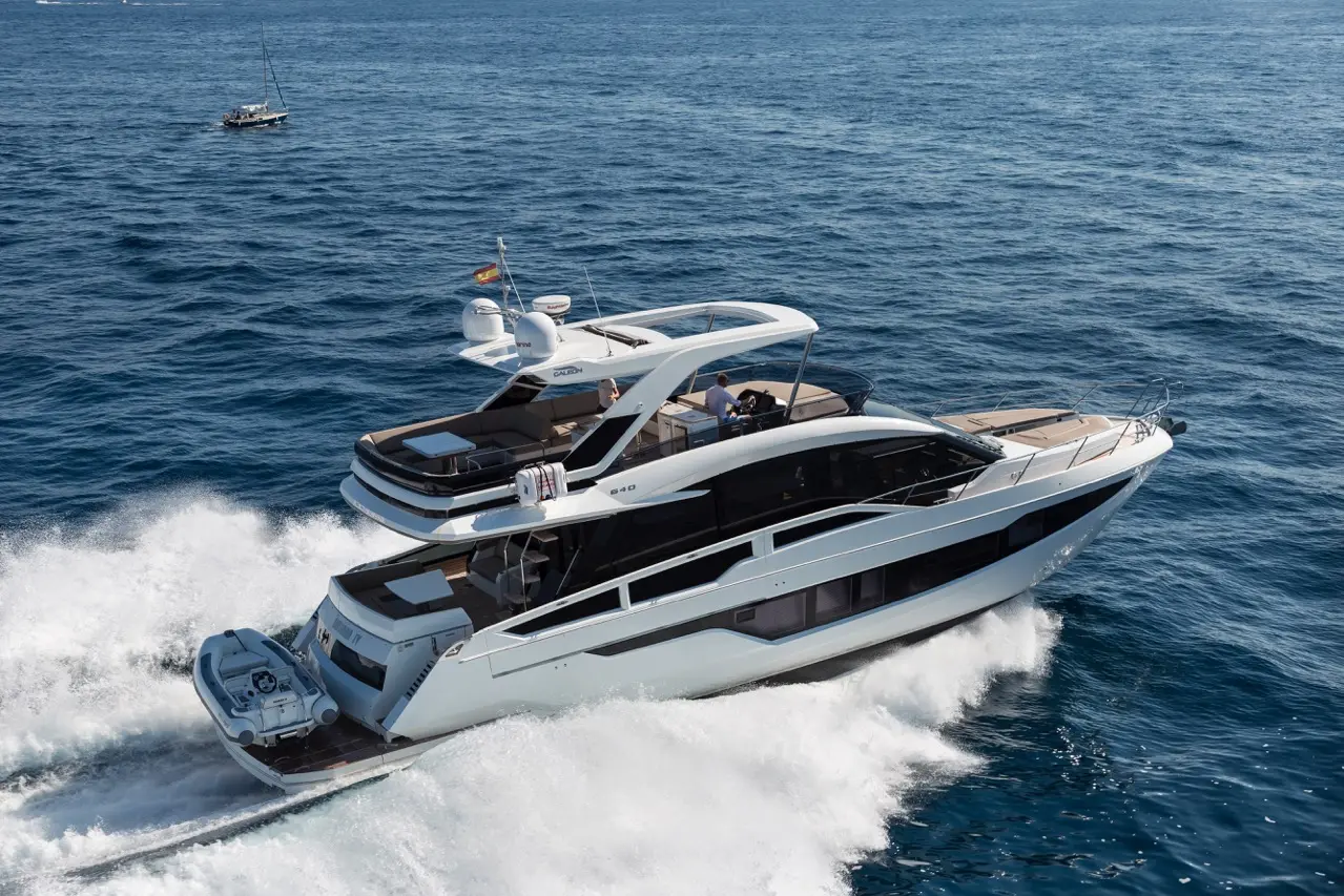 A luxury motor yacht glides over blue ocean waves, showcasing sleek design and spacious top deck with sun loungers.