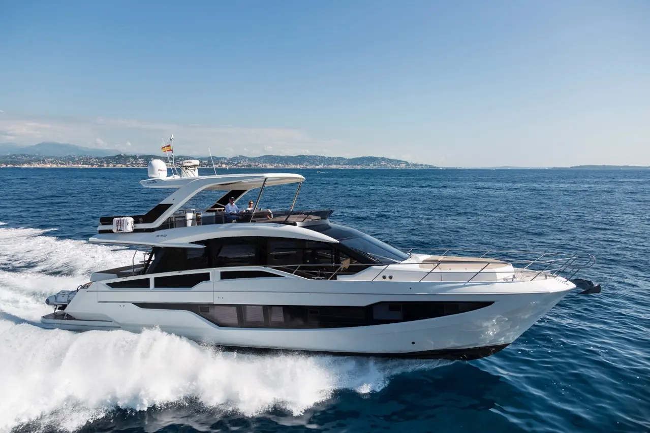 Luxury yacht cruising on blue waters near a coastline, with a sunny sky above and waves splashing against its hull.