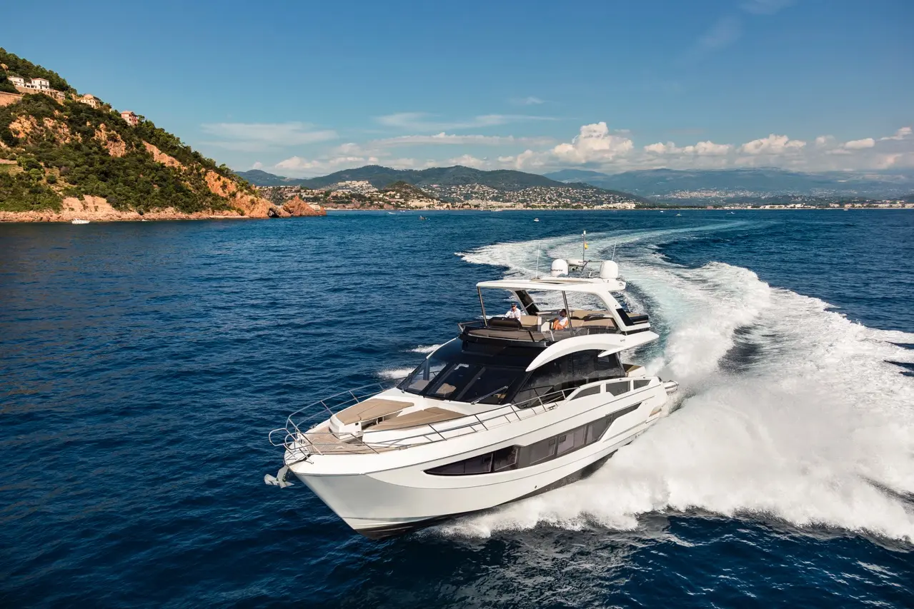 A sleek, white luxury yacht cruising through clear blue waters near a mountainous coastline under a sunny sky.