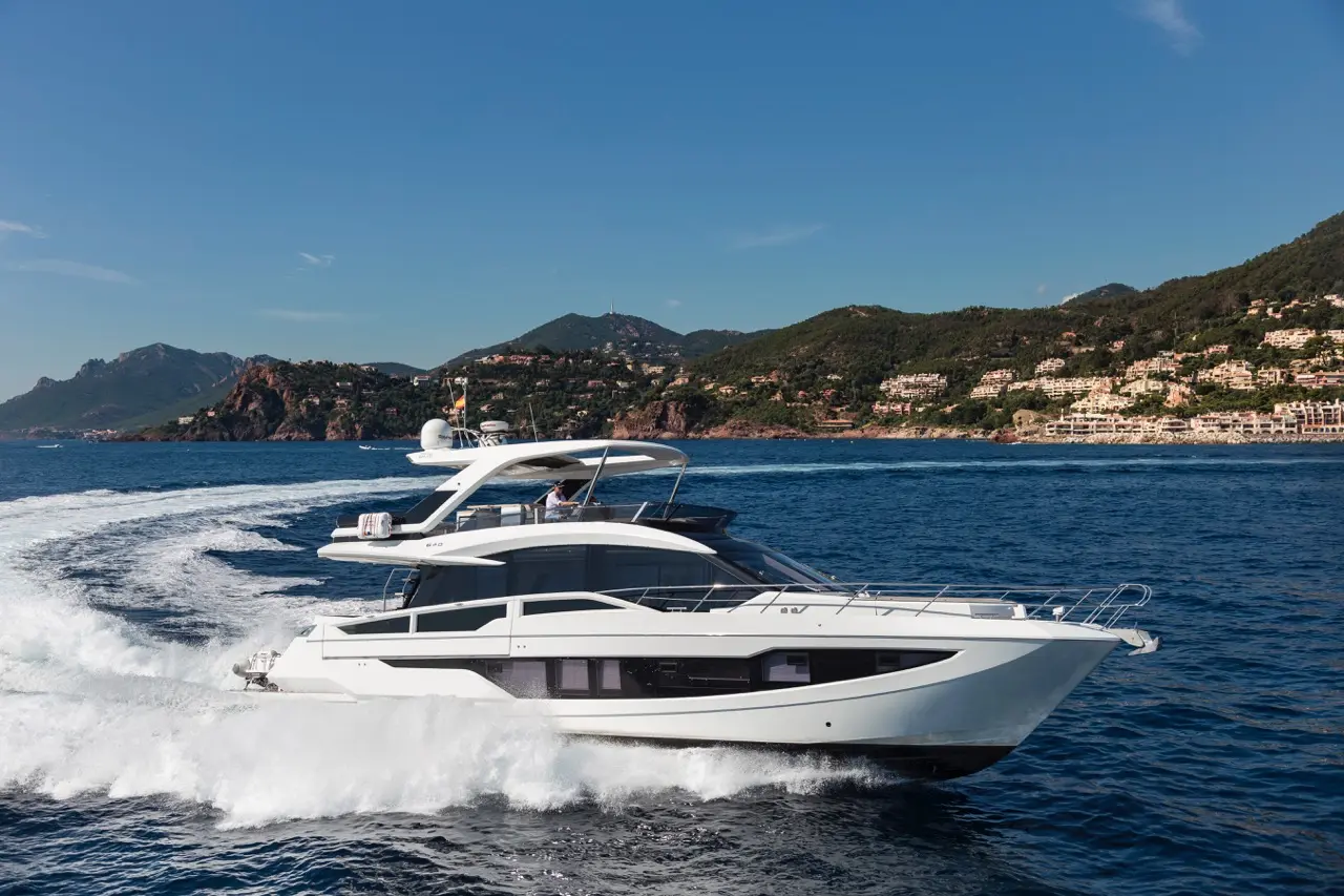Luxury motor yacht cruising through calm blue waters with a scenic mountainous coastline in the background.