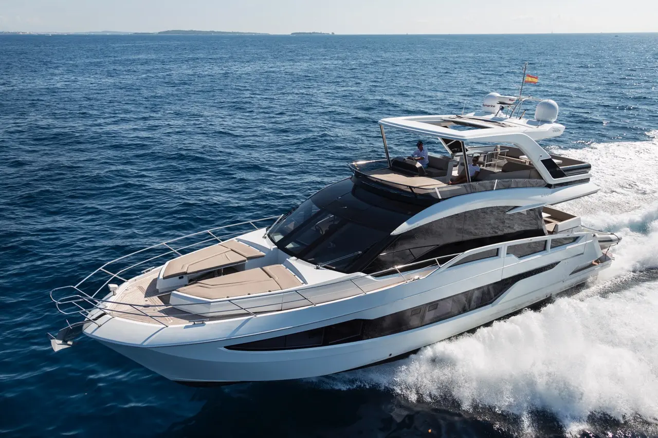 Luxurious yacht cruising on blue waters with a captain at the helm, showcasing sleek design and inviting deck space.