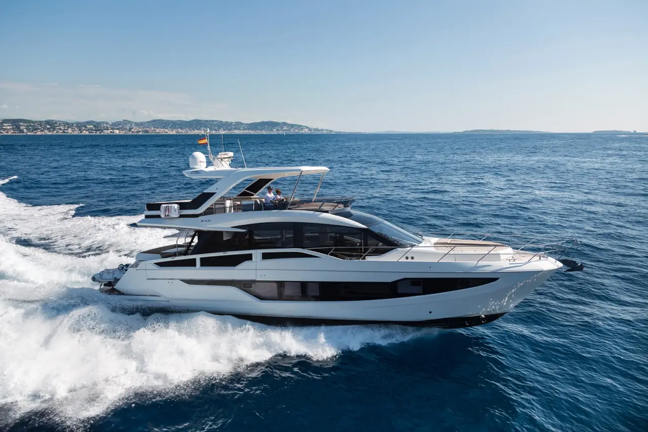 Luxury motor yacht cruising through blue waters with a coastline in the background, showcasing elegance and modern design.