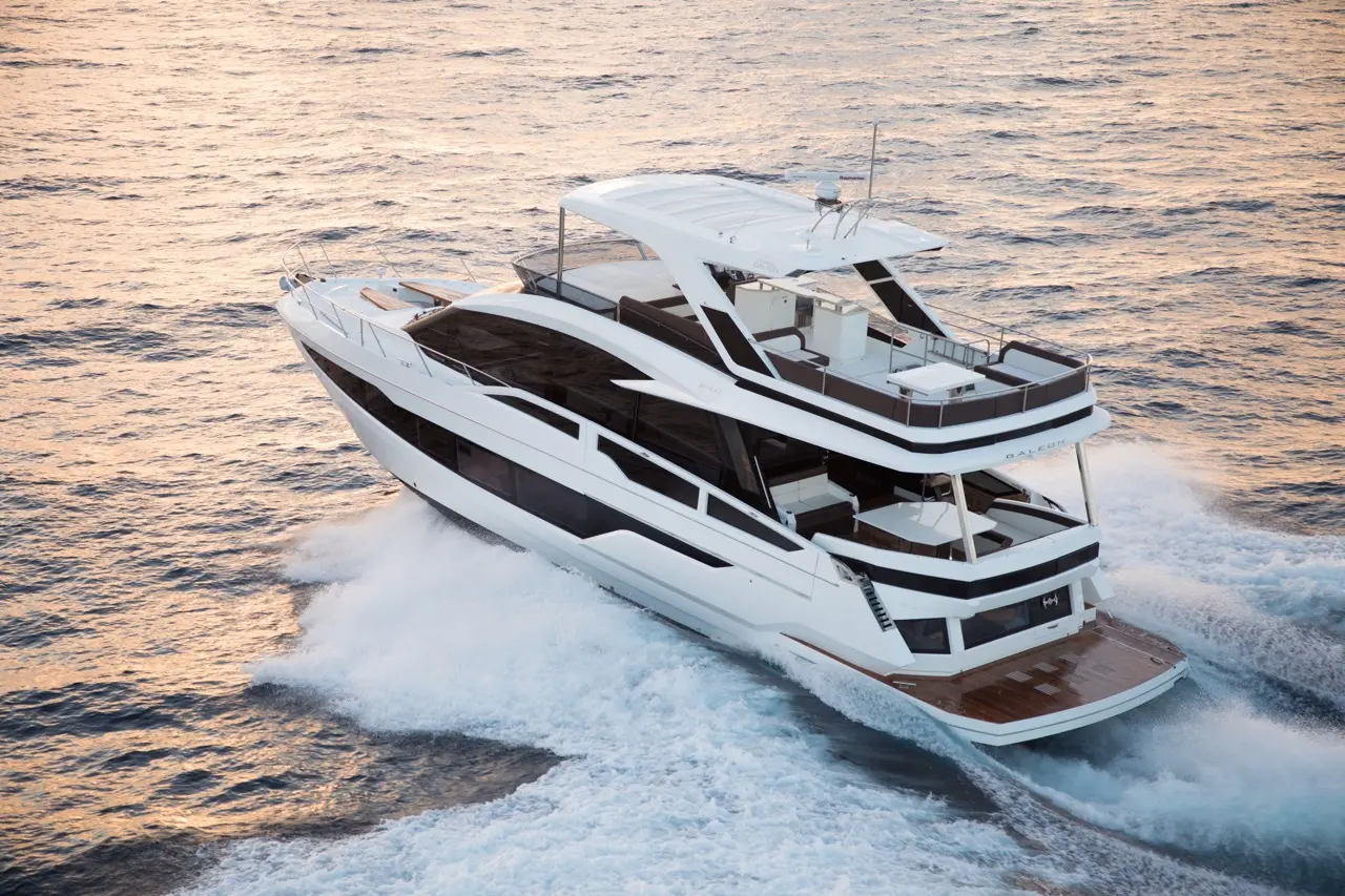 A luxury yacht speeds through shimmering waters, showcasing sleek design and spacious upper deck in a sunset setting.
