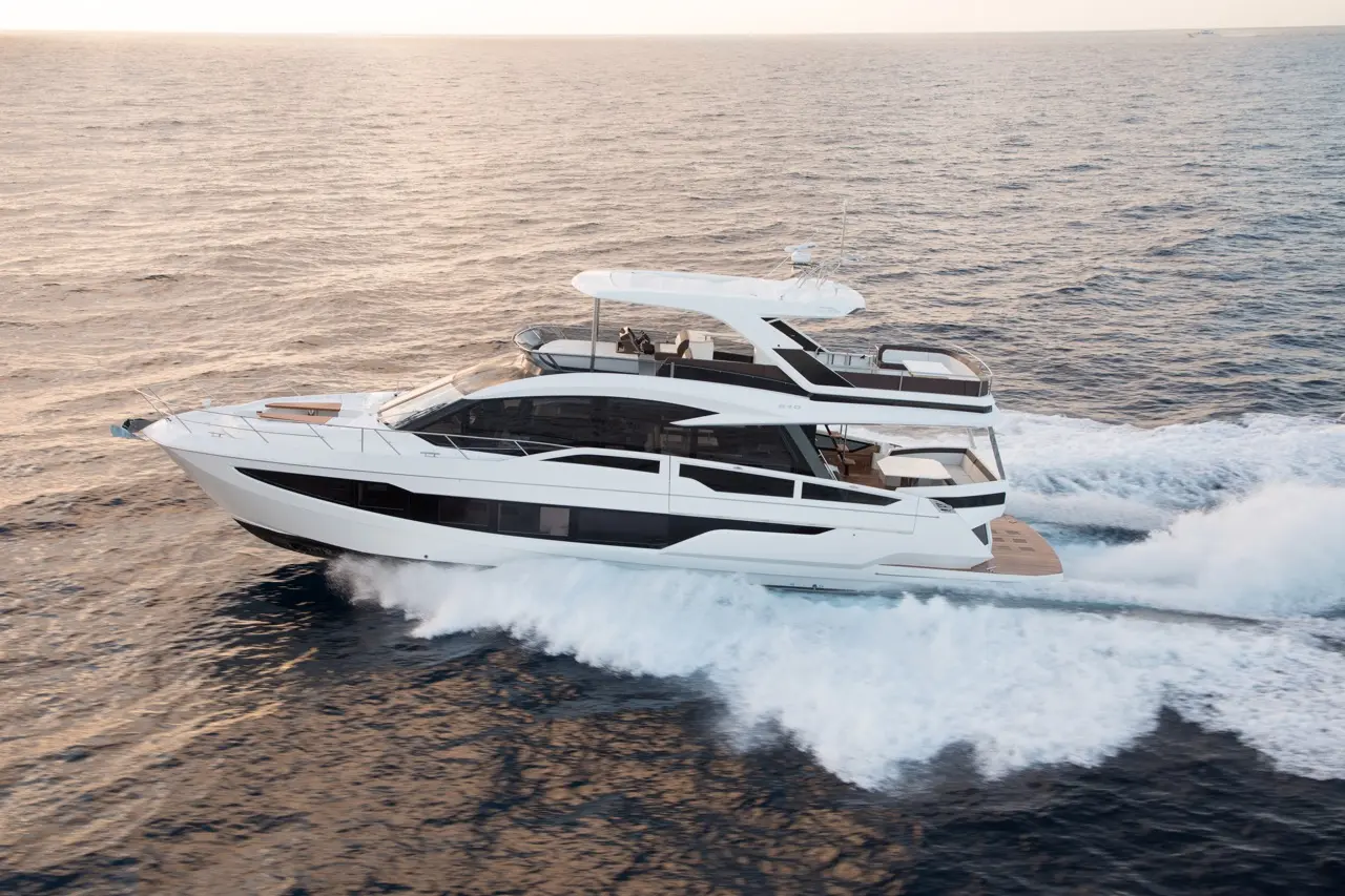A sleek white yacht cruising through the ocean, leaving a frothy wake under a serene sky.