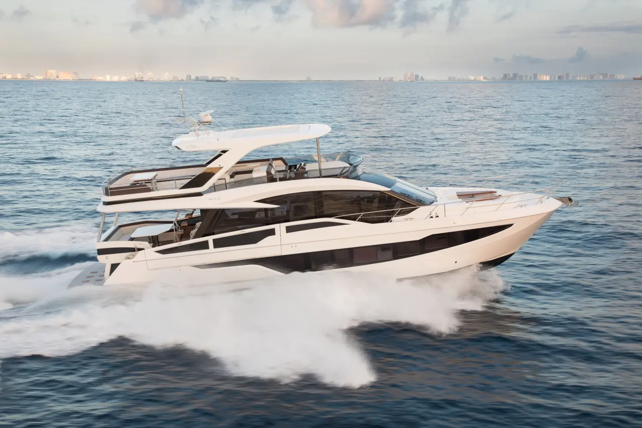 Luxury yacht cruising on clear waters with city skyline in the background, showcasing a modern design and spacious deck.