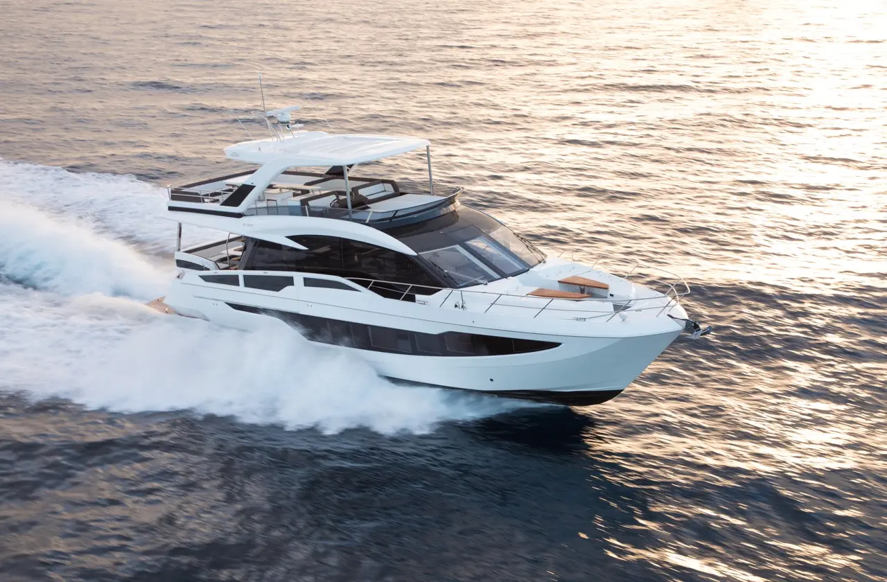 Luxury motor yacht gliding over the water, showcasing sleek design and spacious upper deck against a shimmering sea backdrop.