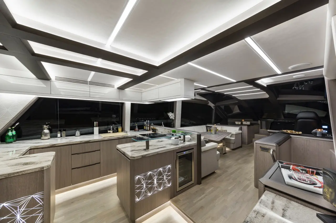 Sleek yacht kitchen featuring modern cabinetry, a minimalist dining area, and illuminated details, with panoramic night views.