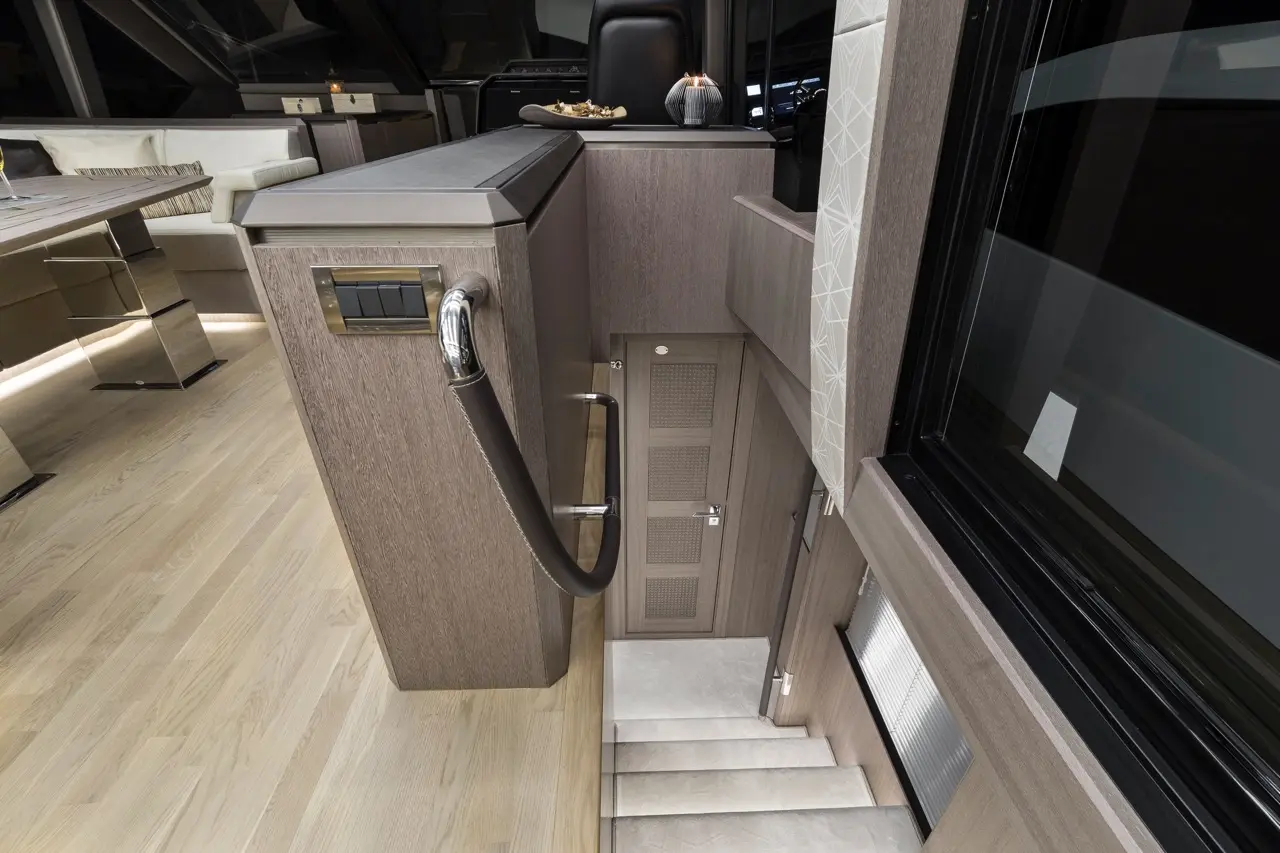 Interior view of a modern yacht staircase with sleek wooden panels, a handrail, and a door leading to another level.