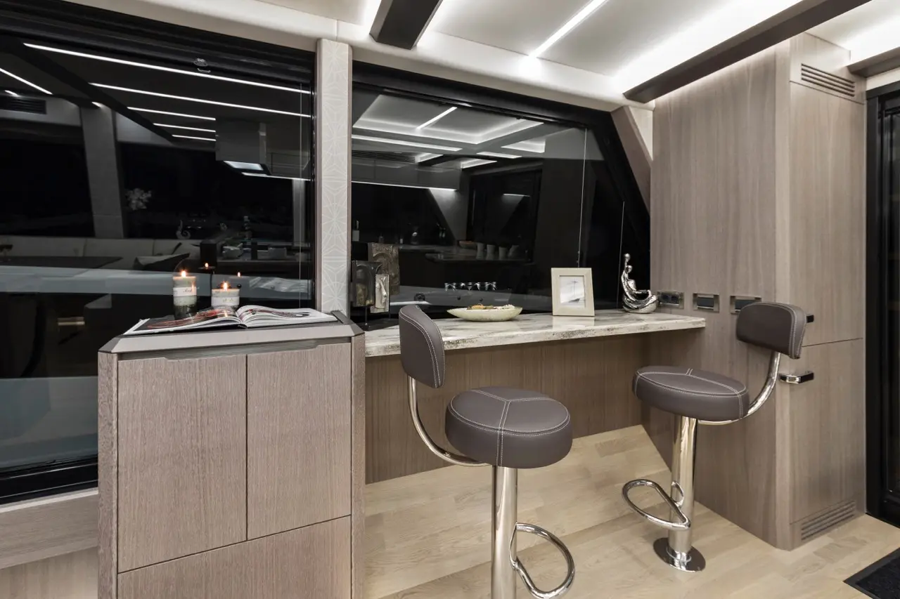 Modern yacht interior with high counter, two bar stools, candles, and a view through large windows, showcasing elegance and comfort.