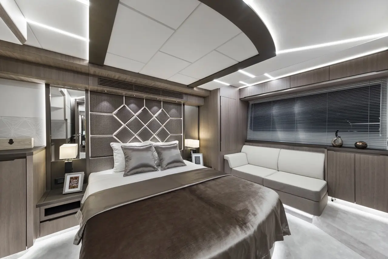 Modern bedroom with a king-sized bed, plush pillows, accent lighting, and a sofa by a window, creating a luxurious ambiance.