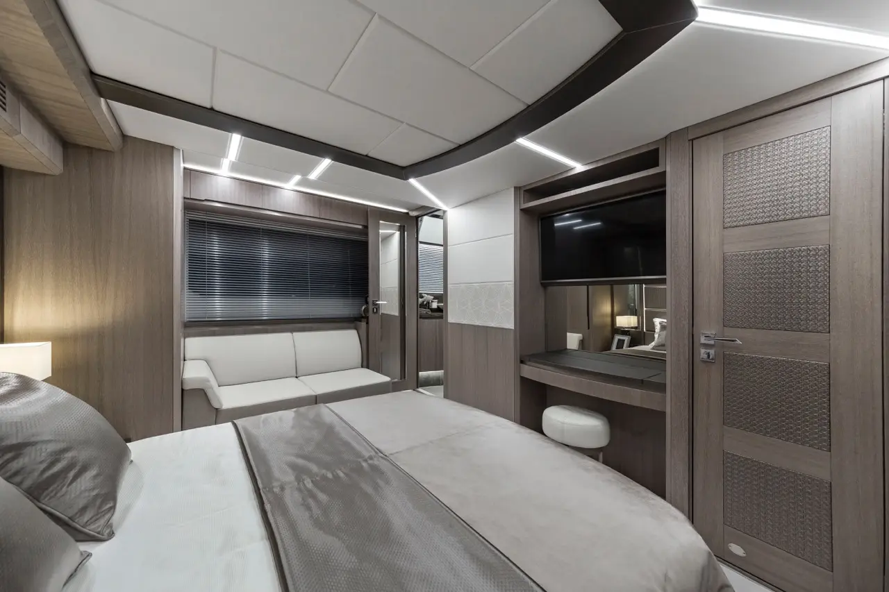 Modern interior of a stylish cabin featuring a double bed, lounge area, desk with a TV, and large windows with blinds.