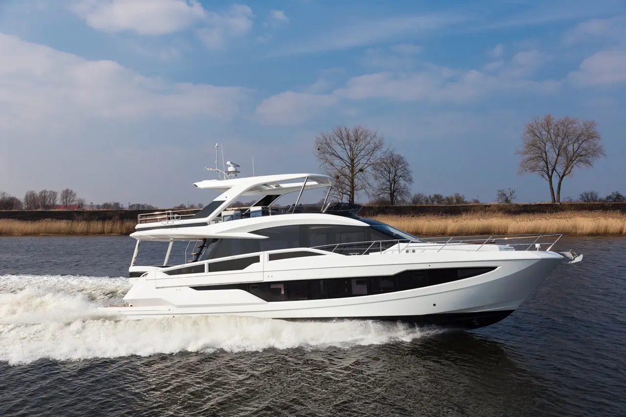 Luxury motor yacht cruising on a calm river, surrounded by trees and grassland, under a clear blue sky.