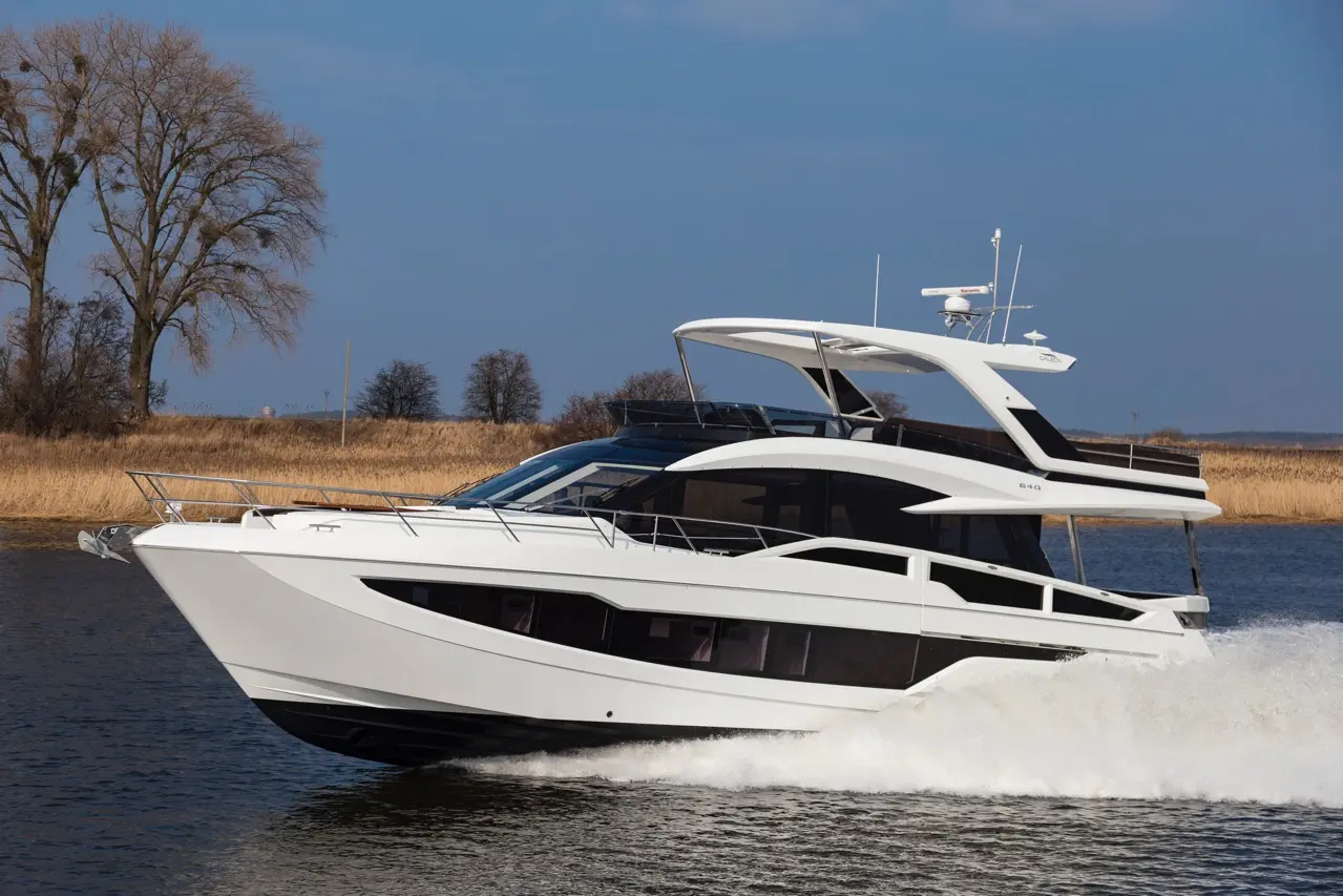 Luxury white motor yacht cruising on water, with a clear blue sky and trees in the background.