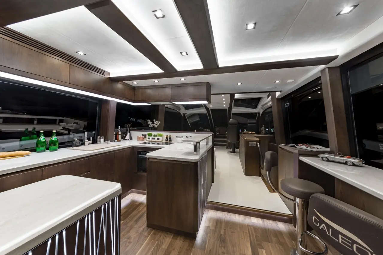 Stylish yacht kitchen with sleek cabinetry, marble countertops, and ambient lighting, featuring a view of the night sea.