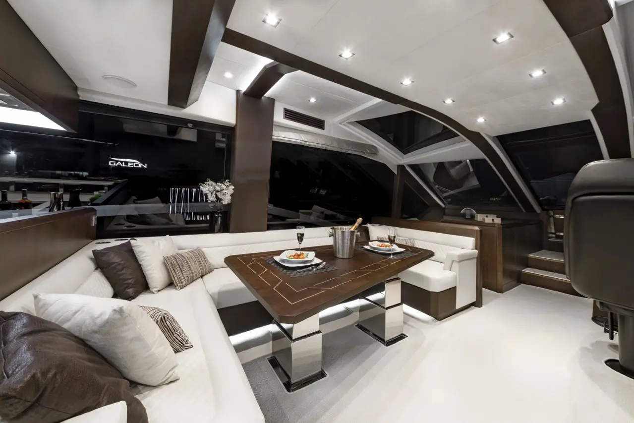 Luxurious indoor yacht dining area featuring plush seating, a polished table with food, champagne, and a large window.