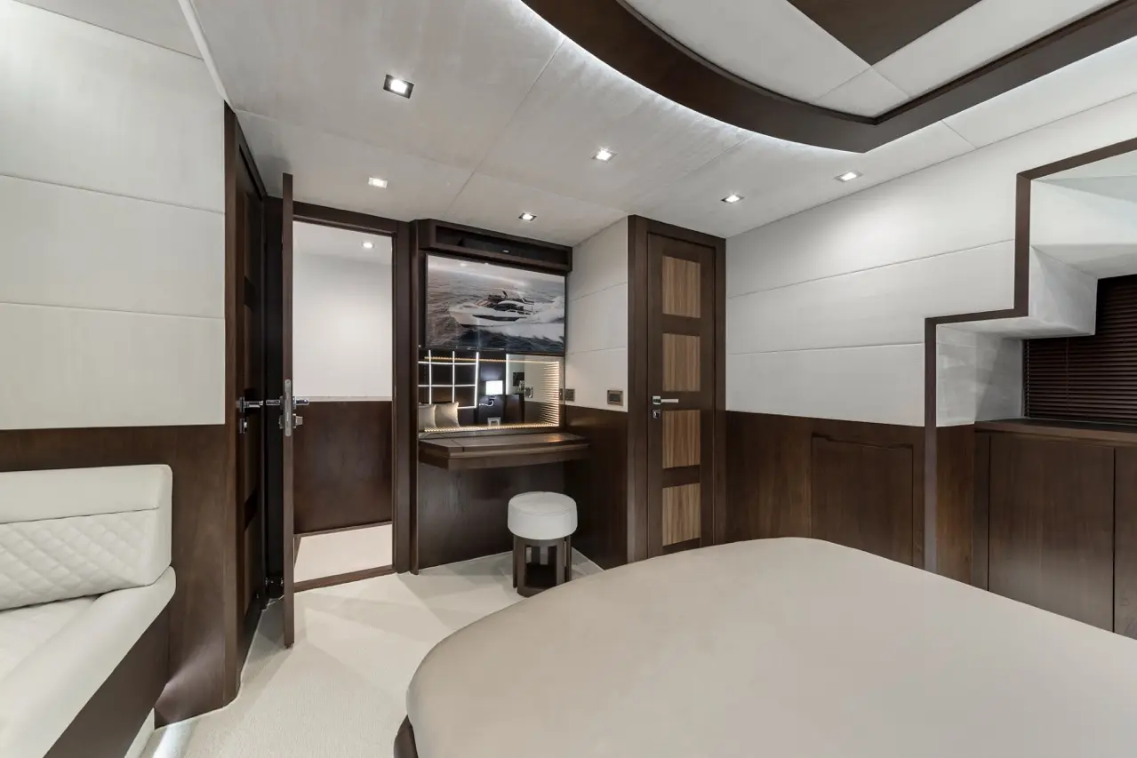 Modern yacht interior featuring a soft beige bed, wooden accents, a desk, and a mirrored wall with nautical artwork.