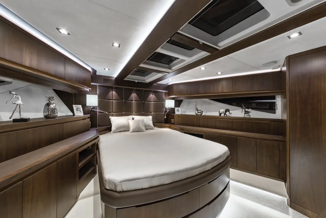 Luxurious yacht bedroom featuring a round bed, wooden furnishings, ambient lighting, and decorative sculptures on shelves.