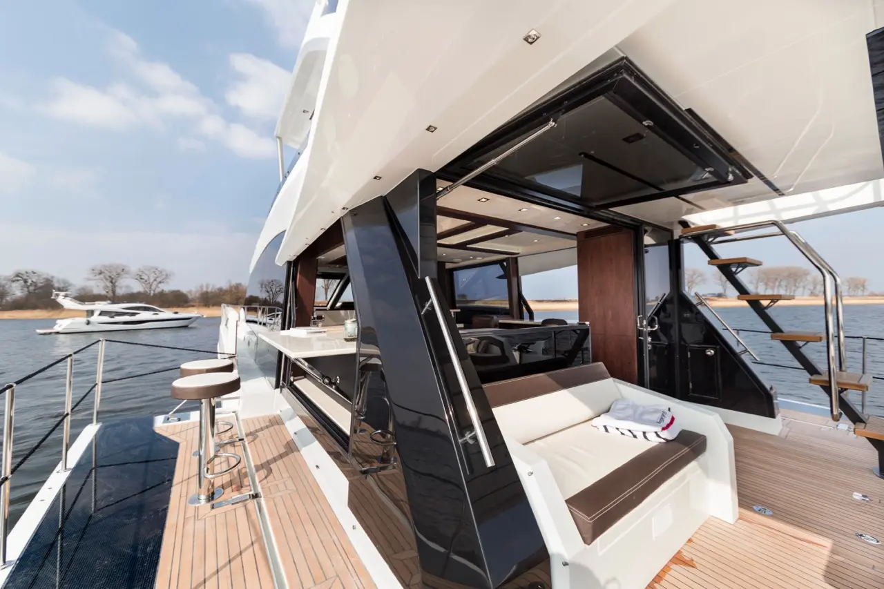 Luxury yacht deck with modern furniture, large windows, and views of the water and another boat in the background.