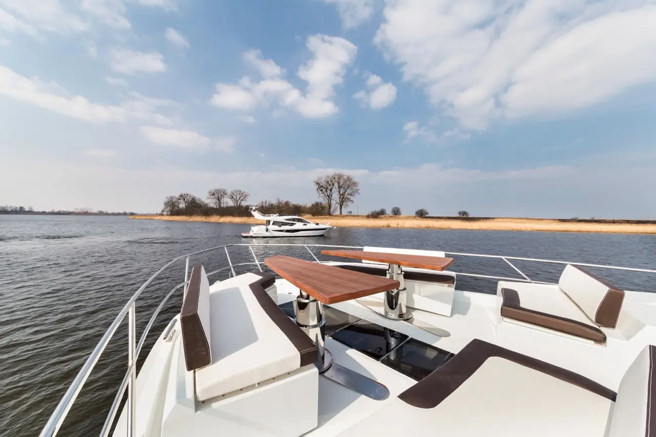 Luxury boat deck with stylish seating, waterway view, and a yacht cruising in the distance under a partly cloudy sky.