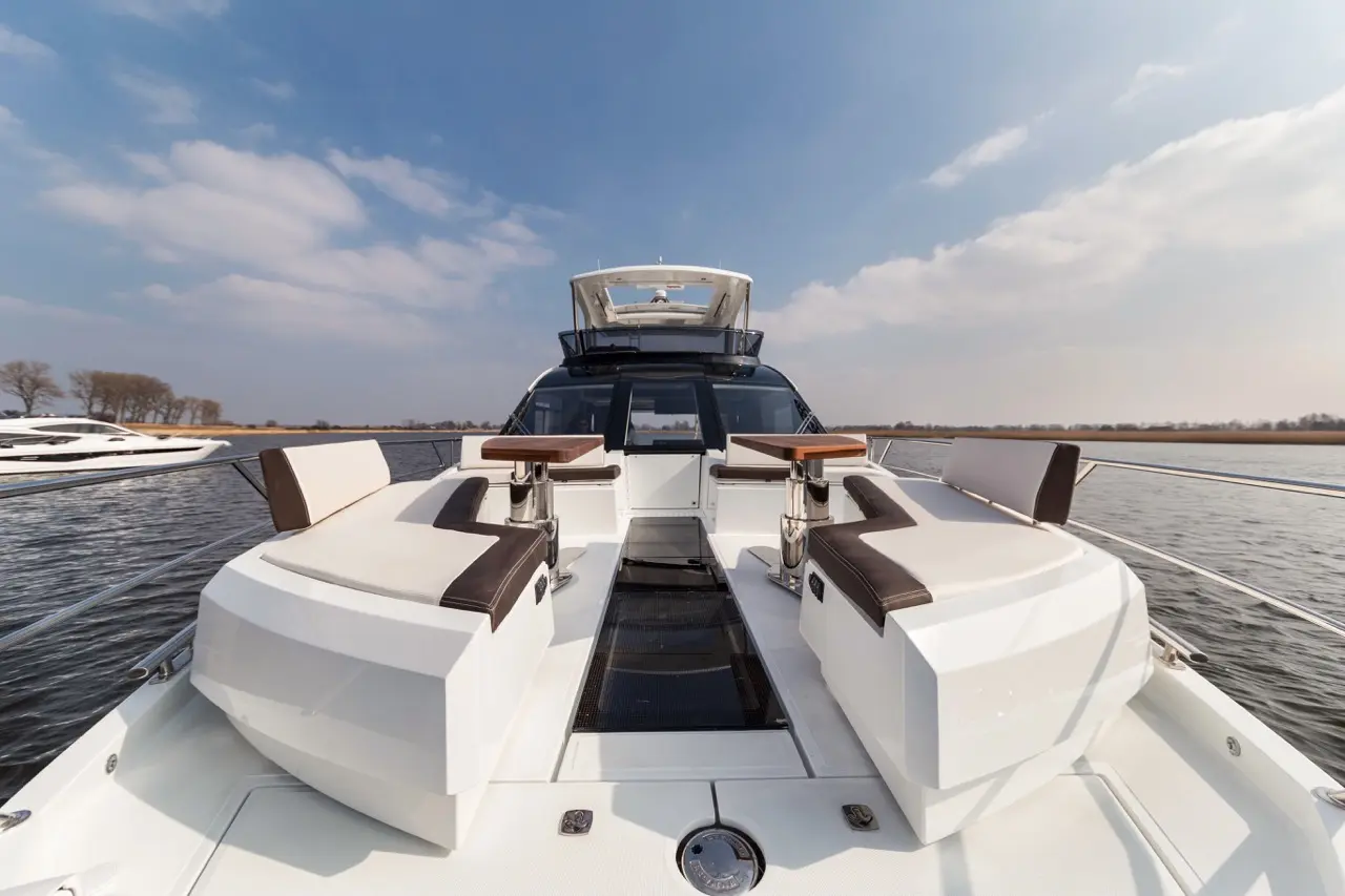 Luxury motor yacht interior featuring plush seating and small tables, set against a tranquil water backdrop under a blue sky.