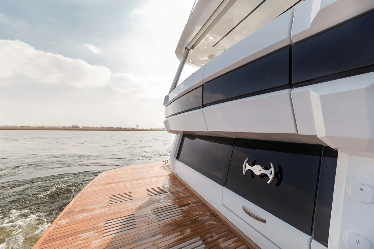 Sleek yacht side view with wooden deck, contrasting white and black panels, and a silver handle against a serene water backdrop.