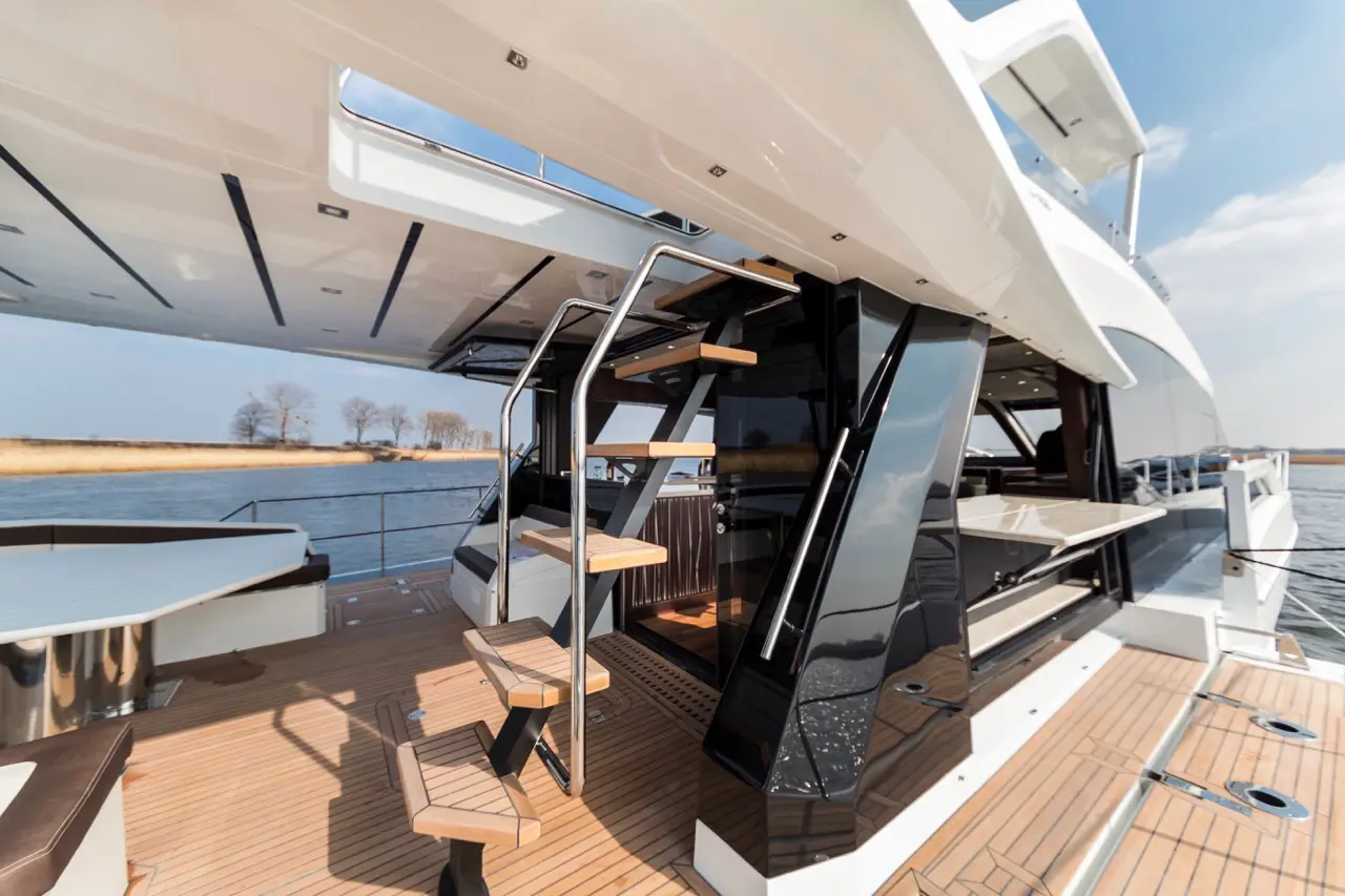 Luxury yacht interior featuring sleek stairway, modern design, polished wood deck, and scenic water view.